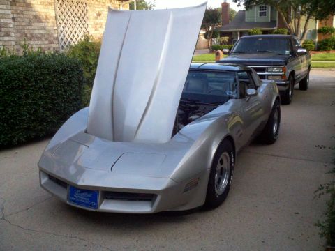 1982 Chevrolet Corvette - Silver 1982 Chevrolet Corvette with hood open, parked behind a black pickup truck.