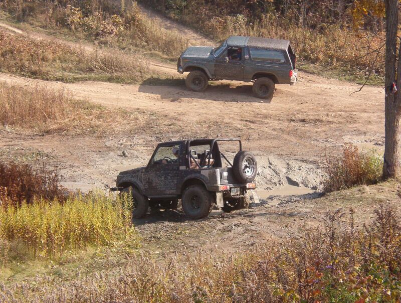 Dark Ford Bronco and muddy small SUV in dirt off-road mud pit