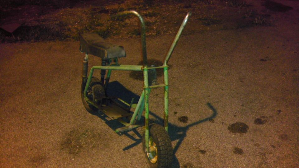 Green mini bike with a black seat and chrome handlebars parked on asphalt