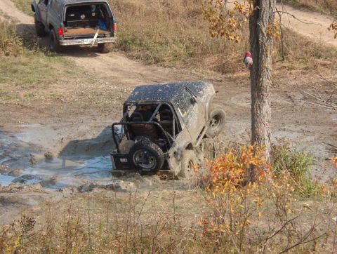 1986 Ford Bronco - Off-road vehicles navigate a muddy trail, with one vehicle deeply stuck in the mire.