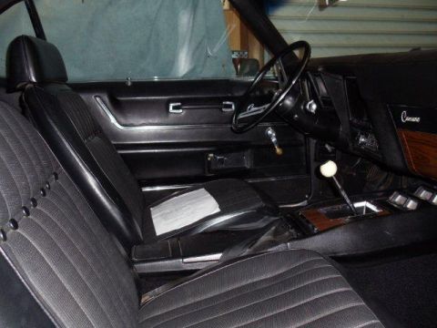 1969 Chevrolet Camaro - The interior of a 1969 Chevrolet Camaro features black vinyl seats, wood grain trim, and a prominent Camaro badge on the dashboard.