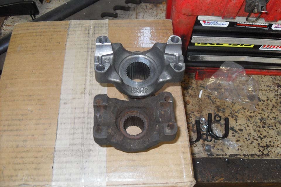 New and old driveshaft yokes side-by-side on a cardboard box. Hardware is scattered nearby