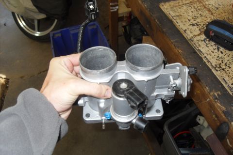 1997 Ford Ranger - A hand holds a silver dual throttle body, a critical engine component, against a workshop background.