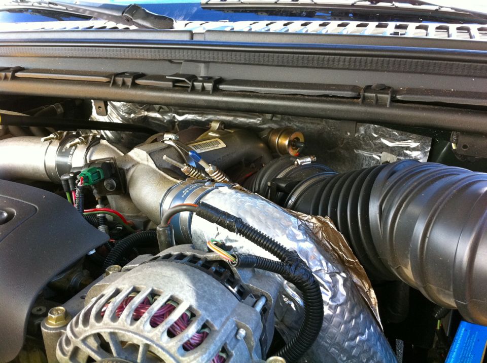 Diesel engine bay close-up: aluminum intake elbow, foil heat wrap, black intake boot and alternator