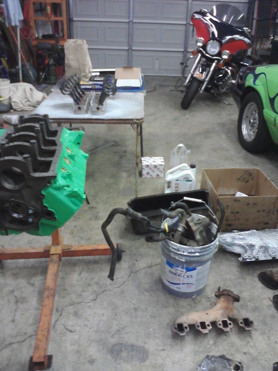 Engine block on stand, motorcycle, and various car parts in a garage