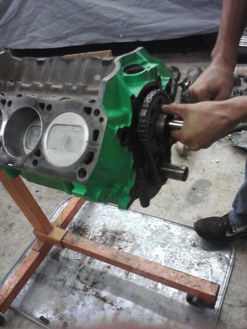 1989 Ford Bronco - Hands are shown working on the timing chain and gears of a green-painted engine block.