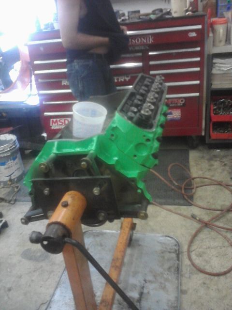 1989 Ford Bronco - A green engine block is mounted on an orange engine stand in a workshop setting.