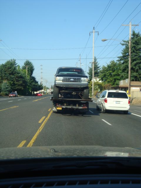 1989 Ford Bronco - A 1989 Ford Bronco is seen from the front, driving on a road with another vehicle to its right.