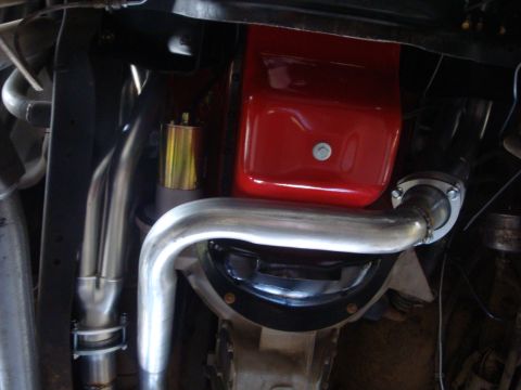 1989 Ford Bronco - Underside view of a vehicle's engine and exhaust system, a red valve cover and polished exhaust pipes.