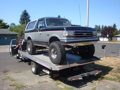 1989 Ford Bronco - Ford Bronco being loaded onto a tow truck, showing its lifted suspension and large tires.