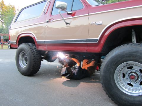 1984 Ford Bronco - A person welds underneath a lifted Ford Bronco, which appears to be from the early 1980s.