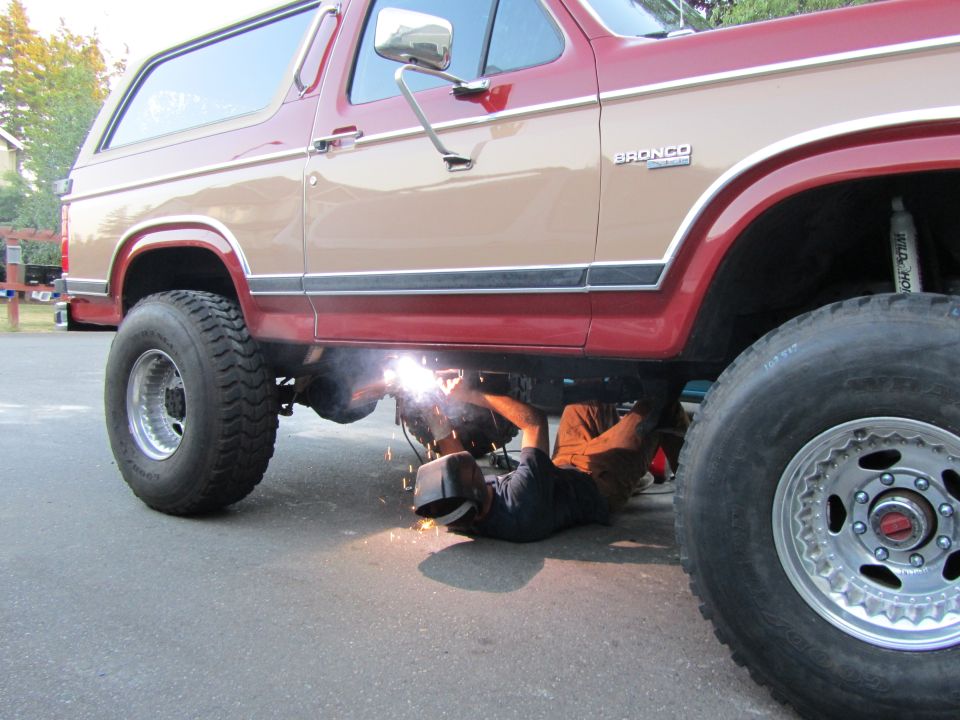 Two-tone red and tan Ford Bronco with a person welding underneath