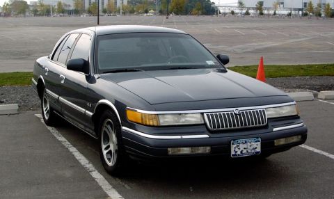 1999 Ford Crown Victoria - A dark sedan is parked in an empty lot with an orange traffic cone nearby.