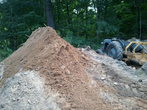 1985 Ford F-150 - A tractor and grader are positioned near a large pile of dirt, with trees in the background.