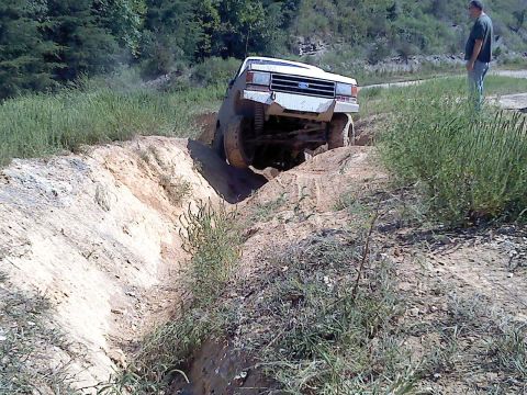1989 Ford Bronco - A white off-road vehicle with a lifted suspension navigates a challenging dirt ditch during an outdoor event.