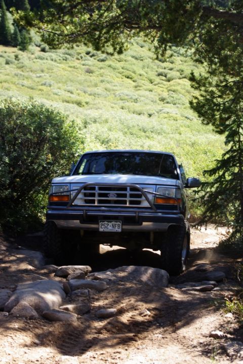 1996 Ford Bronco - White Ford Bronco navigates a rocky, wooded trail.