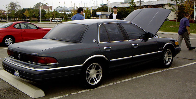 Dark sedan with hood open, rear quarter view. Appears to be a Mercury Grand Marquis