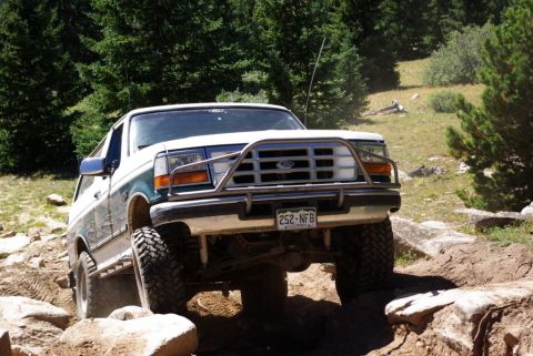1996 Ford Bronco - This Ford Bronco is shown off-road on a sunny day with trees in the background.