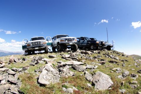 1996 Ford Bronco - Several SUVs are parked on a rocky mountain peak with a clear blue sky above.