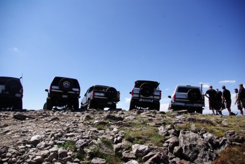 1996 Ford Bronco - Several SUVs, including a 1996 Ford Bronco, are parked on a rocky hillside under a bright blue sky.