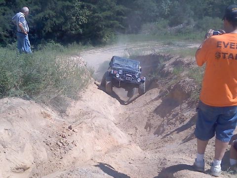 1989 Ford Bronco - A Jeep navigates a challenging off-road trail while onlookers observe and document the event.