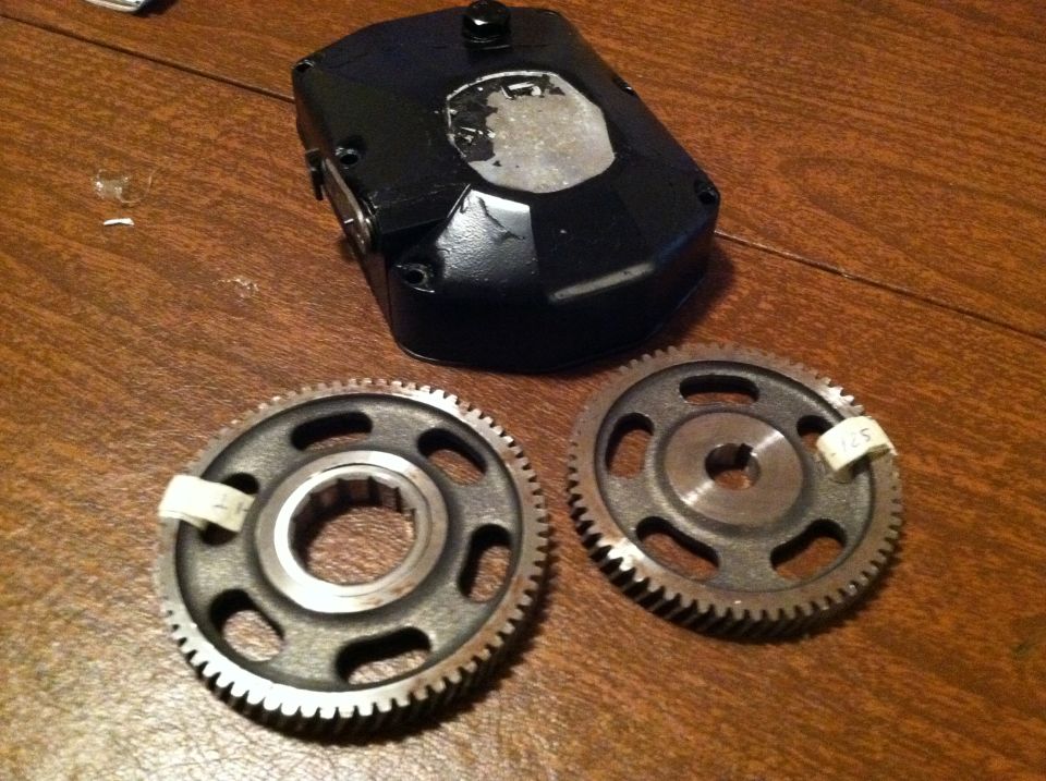 Two metal gears with teeth and a black housing with a clear patch on a wooden surface