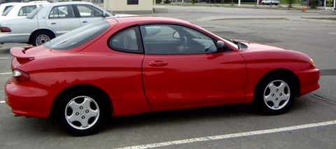 1999 Ford Crown Victoria - A red coupe is parked in a lot, with a silver sedan behind it.