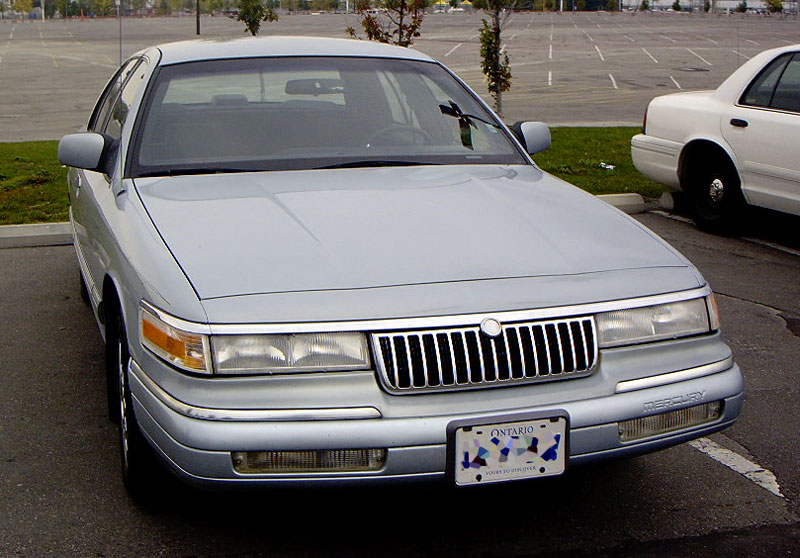 Silver Mercury Grand Marquis parked in a lot, with a white police car in the background. Ontario license plate visible