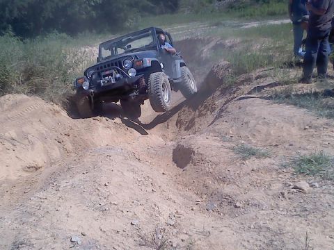 1989 Ford Bronco - A black Jeep Wrangler navigates a steep dirt obstacle during an off-road event.