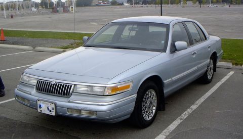1999 Ford Crown Victoria - A light blue Mercury Grand Marquis is parked in a lot, showing its front three-quarter view.