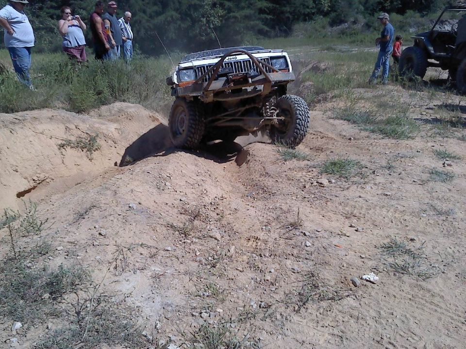White Jeep Cherokee XJ climbing a dirt hill with people watching