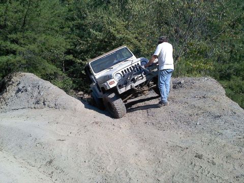 1989 Ford Bronco - Man attempts to navigate a white Jeep Wrangler TJ up a steep dirt embankment.