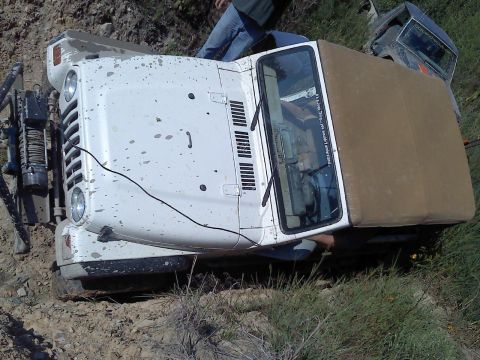 1989 Ford Bronco - A white Jeep Wrangler is stuck on a dirt incline, with another vehicle partially visible behind it.