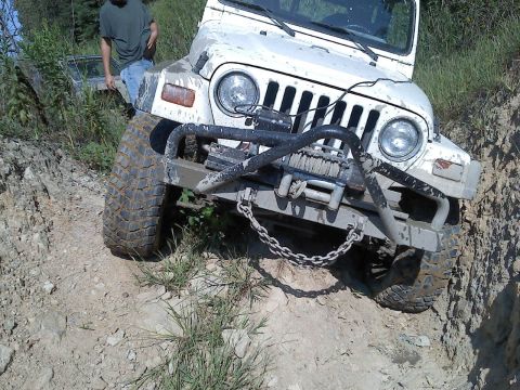 1989 Ford Bronco - A white Jeep Wrangler navigates a challenging dirt trail with a winch attached to its front bumper.