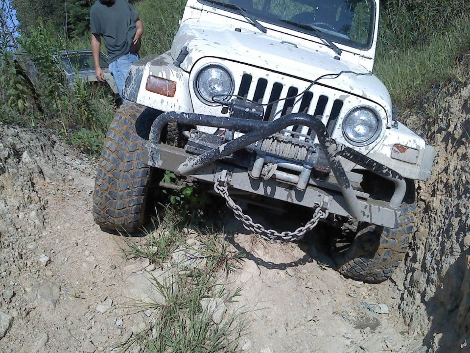 White Jeep Wrangler with winch on front bumper, tires covered in mud, on a dirt trail