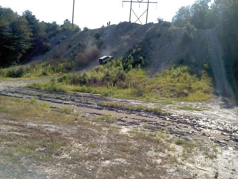 1989 Ford Bronco - A white SUV navigates a challenging muddy incline on a sunny day, with power lines visible against the sky.