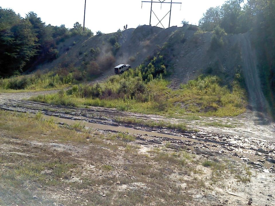 White SUV driving up a muddy hill with power lines overhead