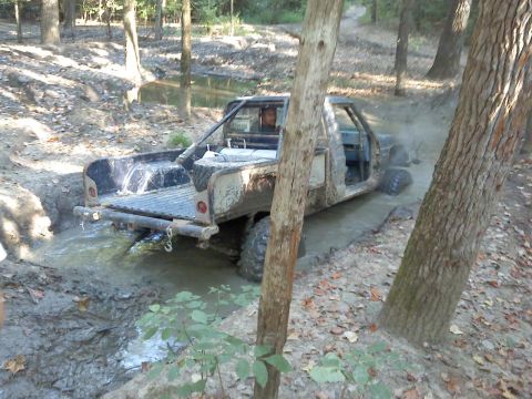 1989 Ford Bronco - A modified pickup truck navigates a challenging off-road trail, kicking up mud as it goes.
