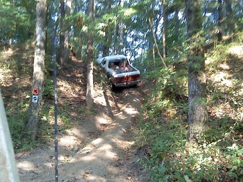 1989 Ford Bronco - A white pickup truck navigates a challenging off-road trail through a dense forest.
