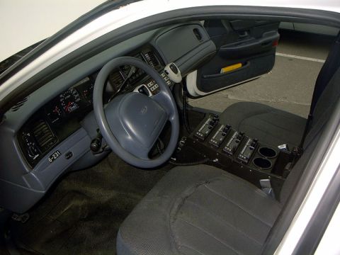1999 Ford Crown Victoria - The interior of a 1999 Ford Crown Victoria police car is visible, the dashboard, steering wheel, and a specialized center console with mult…