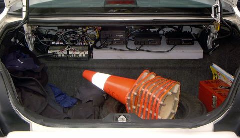 1999 Ford Crown Victoria - Trunk of a vehicle filled with electronic equipment and traffic cones, including a spare tire.