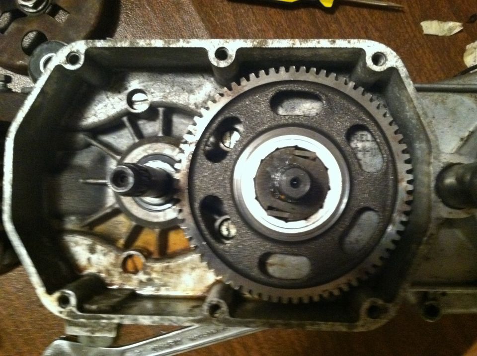 Close-up of moped transmission gears inside a casing. A wrench is visible below