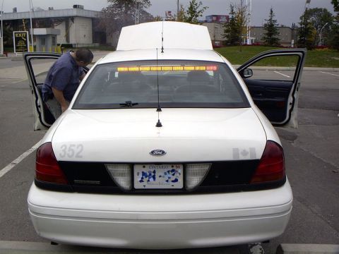 1999 Ford Crown Victoria - A white 1999 Ford Crown Victoria police car is shown with its doors open and hood raised, parked in a lot.
