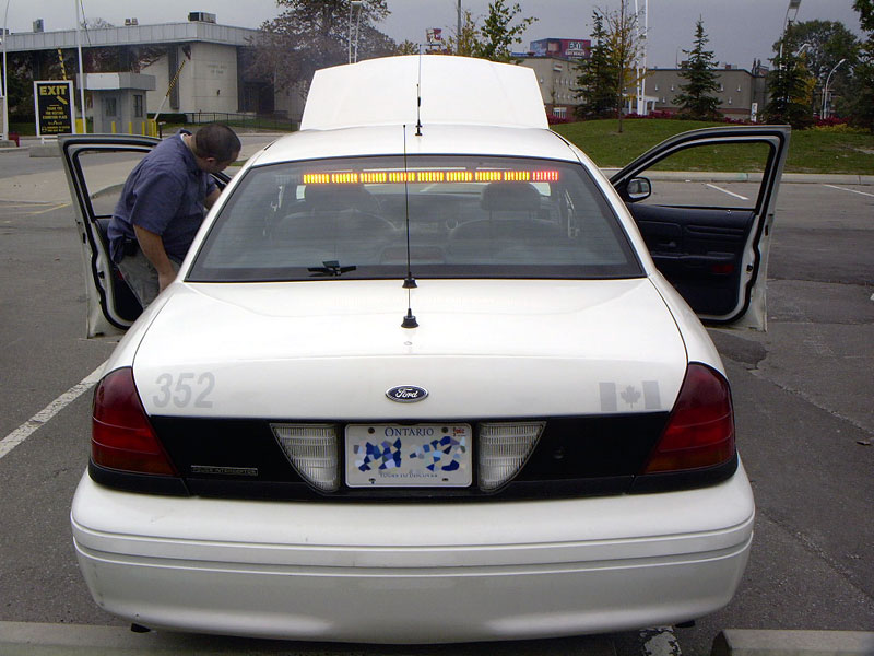 Rear of a white 1999 Ford Crown Victoria police car with doors open and hood up. Ontario license plate visible