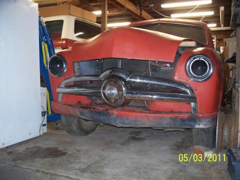 1990 Ford Bronco - A red classic car sits in a garage, its front end exposed, with another vehicle in the background.