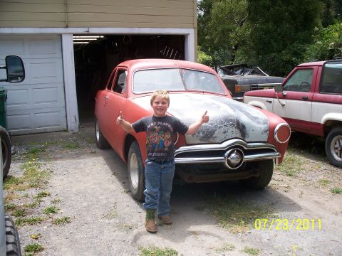 1990 Ford Bronco - A young boy poses with a classic car in front of a garage, with other vehicles visible.