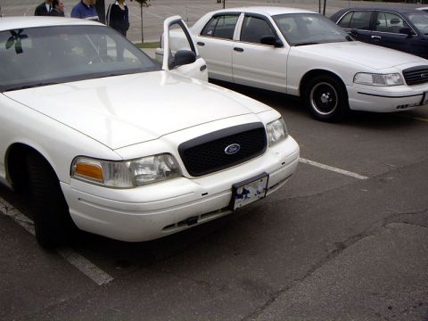 1999 Ford Crown Victoria - Two white Ford Crown Victorias are parked side-by-side in a parking lot.