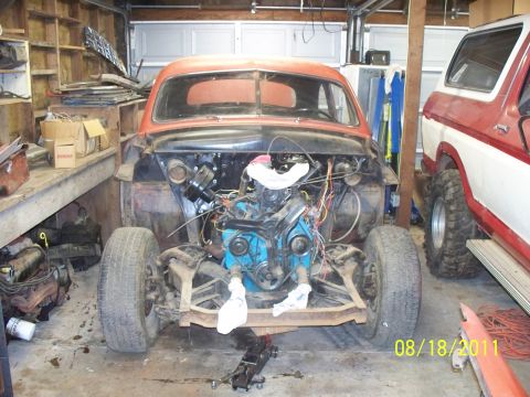 1990 Ford Bronco - A vintage car is undergoing repairs in a garage, with a Ford Bronco parked nearby.
