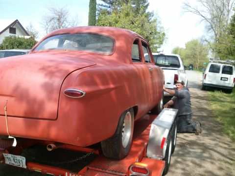 1990 Ford Bronco - Man secures red sedan to trailer, with other vehicles nearby.