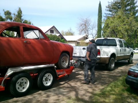 1990 Ford Bronco - A red coupe is loaded onto a trailer, with a white pickup truck hitched behind it.